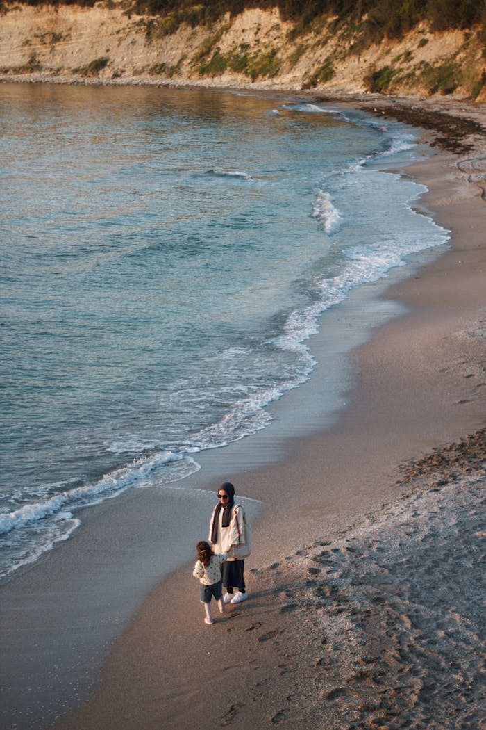A mother and daughter walk along a tranquil beach at sunset. Perfect for family and travel themes.