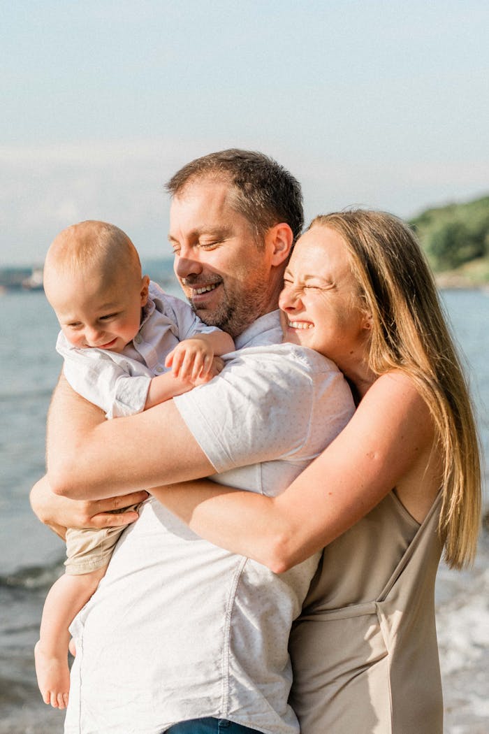 A joyful family shares a warm embrace on a sunny beach day.