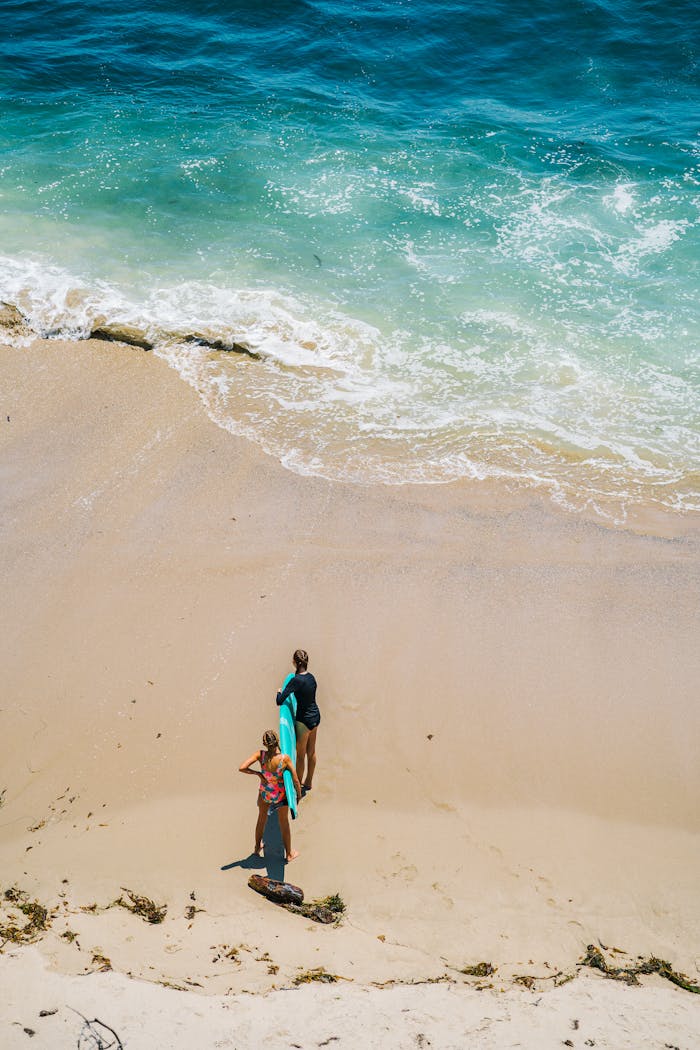 High-angle shot of surfers holding boards on a sandy beach by the ocean.